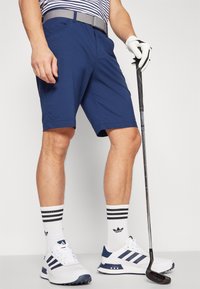 Granatowe szorty golfowe z płaskim przodem, dwiema kieszeniami i wygodnym krojem. W zestawieniu z białymi trampkami i paskowanymi skarpetami sportowymi.