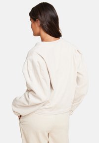 Lys beige kordfløyelsgenser med puffede ermer og rund hals, med subtil tekstur og en avslappet passform. Ingen synlige lukkinger.