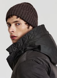 Doudoune gris foncé avec un col montant, une texture matelassée et un cordon de serrage ajustable. Bonnet en maille côtelée marron porté sur la tête.