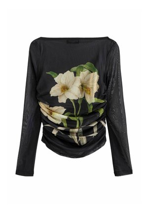 Femme portant un haut noir transparent à manches longues avec un grand imprimé fleur blanche, un pantalon noir taille haute à jambes larges, et des chaussures noires à l'extérieur.