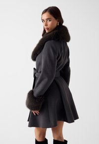 Donkergrijze wollen jas met een brede bontkraag en manchetten, een getailleerde taille, een uitlopende rok en een strak ontwerp. Zachte textuur en elegante silhouet.