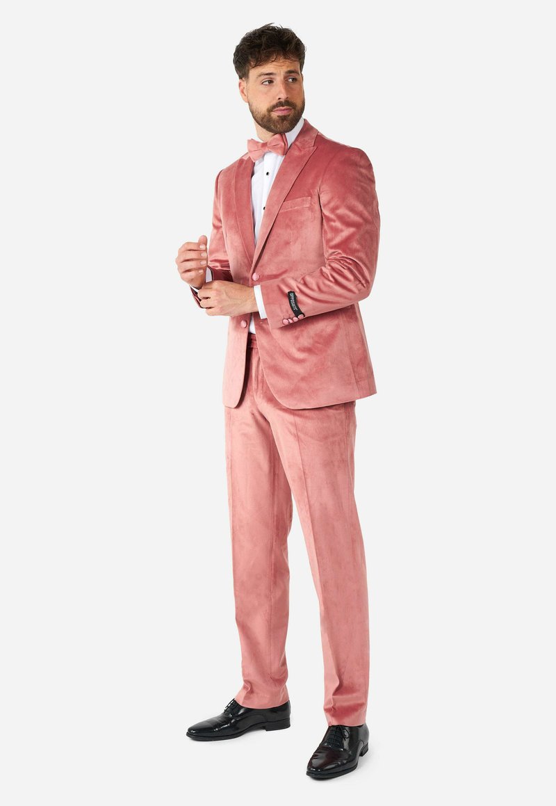 Esmoquin de terciopelo rosa claro con pajarita a juego. Incluye zapatos formales negros, camisa blanca y botones negros en los puños de la chaqueta.
