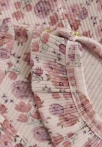Blommönstrad tyg i mjuk rosa med ribbad textur, med olika nyanser av rosor och små gröna accenter. Inkluderar detaljer i guld.