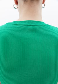 Zelený žebrovaný svetr s těsným výstřihem, texturovanou tkaninou a zjednodušeným designem bez dalších ozdob.