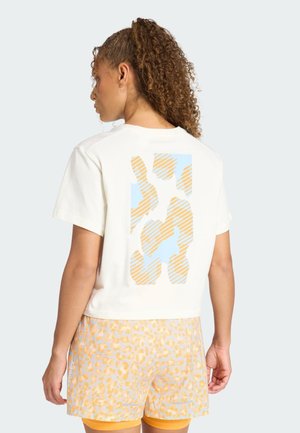 Cremefarbenes T-Shirt mit kurzen Ärmeln, das auf der Rückseite ein blau-orangefarbenes abstraktes Muster zeigt, kombiniert mit hellgelben Shorts mit Leopardenmuster.