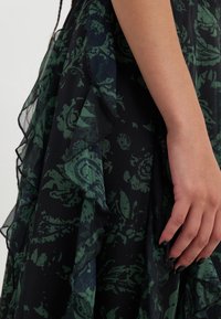 Zwarte sheer jurk met donkergroene bloemenpatronen, met ruches en textiel met een structuur, accentueert een vloeiende uitstraling.