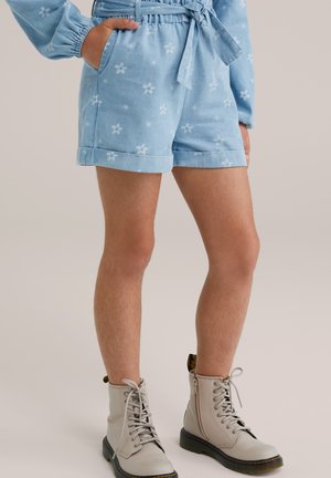 Pantaloni corti azzurri, a fantasia floreale, con vita cinchata e tasche laterali, abbinati a stivali alla caviglia beige con lacci.