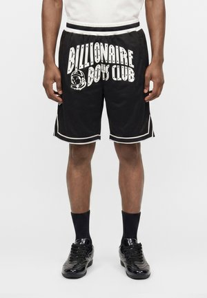 Sorte shorts med hvide kanter og teksten "Billionaire Boys Club" med en astronaut-grafik båret af en person, der står mod en ensfarvet baggrund.