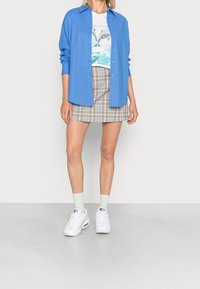 Camicia azzurra chiara a maniche lunghe sopra una t-shirt bianca con stampa di delfini, abbinata a una mini gonna a quadri, sneakers bianche e calzini verde chiaro.