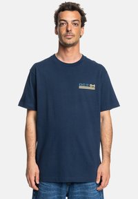 Navy blue cotton t-shirt features a round neckline, short sleeves, and a graphic print in green and yellow on the left chest.