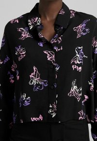 Button-up shirt in black fabric featuring a butterfly pattern in pink, white, and purple. Includes a spread collar and short sleeves.