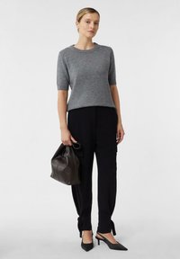 Szary sweter z krótkim rękawem z dzianiny, czarne dopasowane spodnie z bocznymi kieszeniami oraz czarne szpilki z ostrym noskiem. W ręku brązowa skórzana torebka.