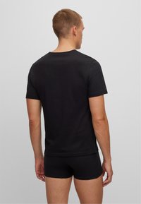 Black short-sleeved t-shirt in cotton, featuring a crew neck and a plain design. Worn with black shorts, viewed from the back.