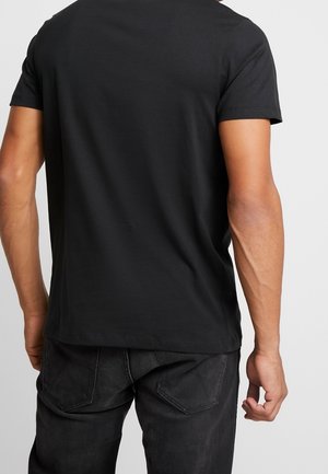 Schwarzes T-Shirt mit kurzen Ärmeln aus Baumwollmischung, mit rundem Ausschnitt und minimalistischem Design, kombiniert mit dunklen Jeans.