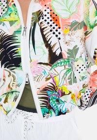 Colorful zip-up bomber jacket featuring tropical leaf and animal prints, with a white base, contrasting dark stripes, and pockets. Lightweight fabric.