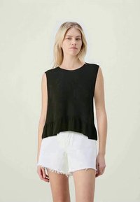 Svart, ribbad ärmlös topp med en utsvängd nederkant, parat med vita fransade shorts. Enkel design, mjuk textur, avslappnad estetik.
