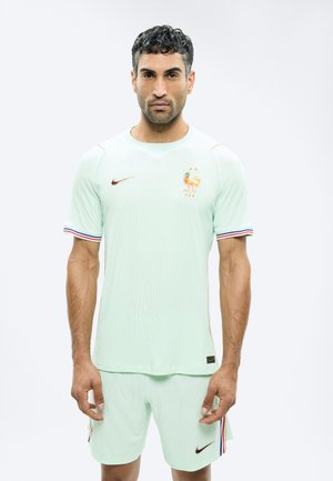 Hombre con uniforme verde claro del equipo nacional de fútbol de Francia, con emblema de gallo y logos de Nike, posando frente a un fondo liso.