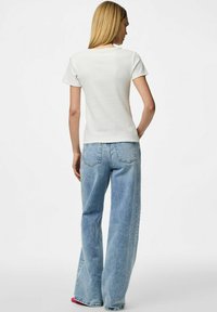 T-shirt blanc à manches courtes en maille côtelée, avec un petit logo sur l'épaule gauche, associé à un jean en denim bleu clair taille haute.