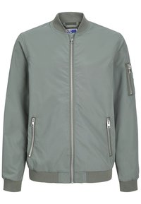 Giacca bomber verde con zip frontale, tasche laterali e tasca con zip sul braccio. Tessuto liscio con polsini e orlo a costine.