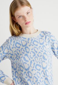 Πουλόβερ λεοπάρ με ανοιχτό κρέμα χρώμα και μπλε βούλες, διαθέτει στρογγυλή λαιμόκοψη και ριμπ μανσέτες. Μαλακή υφή και άνετη εφαρμογή.