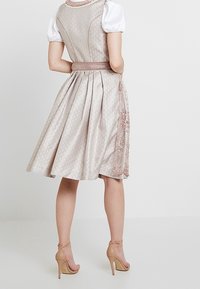 Une robe de couleur pastel, arrivant aux genoux, avec un buste ajusté, une broderie florale le long de l'ourlet et une jupe plissée, associée à des talons beiges.