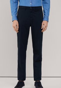 Navyblauwe, slim-fit broek gemaakt van een gladde stof; voorzien van een sluiting met een knoop aan de voorkant en zijzakken; gecombineerd met donkere schoenen.