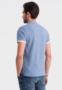 Světle modré polo tričko s krátkými rukávy s bílým lemováním, klasickým límečkem a rovním lemem, kombinované s modrými džínami.