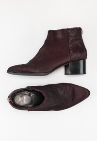 Botas de tobillo burdeos hechas de suave piel sintética, con punta afilada y tacón cuadrado. Presentan un zipper lateral y un forro interior negro liso.
