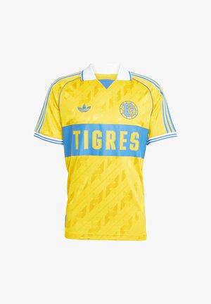 Camisola de futebol amarela com faixa horizontal azul, apresenta o texto "TIGRES", logótipo bordado e detalhes de ombro listrados. Fabricada em tecido suave.