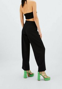 Pantalones anchos negros combinados con sandalias de tacón bloque verde. Las sandalias presentan un diseño de tiras y un acabado texturizado.