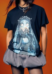 Schwarzes T-Shirt mit einer Illustration eines blauhäutigen Charakters mit langen Haaren, der Blumen hält. Graue, strukturierte Shorts mit einem Bund-Detail.