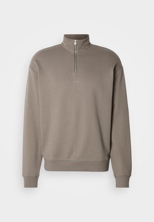 Sudadera con cremallera marrón y cuello alto, puños y dobladillo acanalados. Presenta un pequeño logo en el centro. Fabricada en material suave.