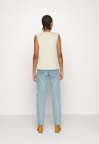 Hellgrauer ärmelloser Pullover mit geripptem Saum, kombiniert mit hellblauen hochgeschnittenen Jeans und tanfarbenen Blockabsatzschuhen. Rückansicht.