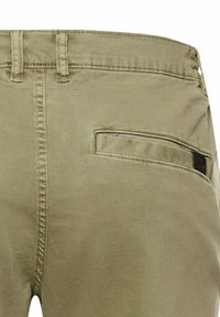 Rückansicht von khakifarbenen Hosen mit Gürtelschlaufen, Mittelnaht und einer einzelnen Leistentasche mit schwarzem Etikett auf der rechten Seite.