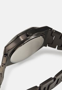 Montre en métal noir avec un boîtier octogonal, une lunette lisse et un bracelet maillon. Elle possède un cadran circulaire réfléchissant et une couronne.