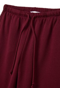 Joggers burdeos con cinturilla elástica, cordón ajustable y tejido suave y elástico; cuentan con tela fruncida en la cintura y un detalle de costura minimalista.