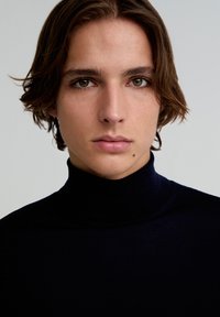 Marinefarbenes Rollkragenhemd aus weichem, dehnbarem Stoff; eng anliegendes Design mit glatter Textur. Das Model hat zerzauste Haare und einen neutralen Gesichtsausdruck.