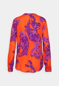 Blouse orange à manches longues avec de grands motifs cachemire violets complexes, visible par l'arrière sur un fond clair uni.
