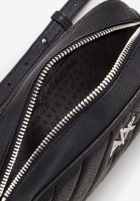 Melna ādas roku soma ar izšūtu faktūru, sudraba rāvējslēdzis un logotipa detaļa. Iekšpusē ir zīmola auduma oderējums.