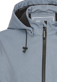 Jasnoniebieska kurtka z kapturem, czarnym suwakiem, regulowanym czarnym ściągaczem oraz widoczną nazwą marki „ILSE JACOBSEN” na suwaku i podszyciu kołnierza.