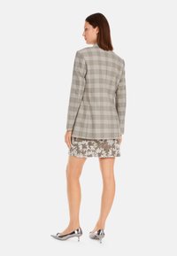 Grau kariertes Blazer mit Spitzrevers, langen Ärmeln und strukturierter Silhouette, kombiniert mit einem floral bestickten Rock und metallischen Absätzen.