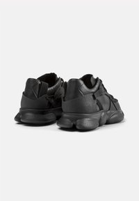 Black sneakers featuring a textured rubber sole, synthetic upper, and padded collar. Design includes minimal stitching and elastic accents.