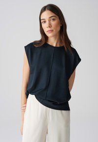 Zwarte mouwloze top van zachte stof, met een ronde halslijn en een relaxte pasvorm, gecombineerd met crèmekleurige, wijde broek.