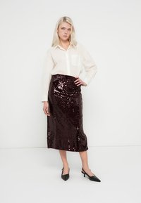 Jupe taille haute bordeaux ornée de sequins avec une texture lisse, associée à une chemise blanche boutonnée et des talons noirs à bout pointu.