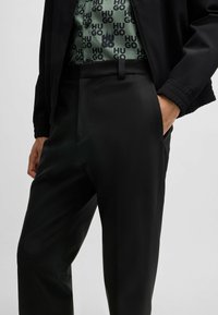 Pantaloni neri su misura in tessuto liscio, caratterizzati da una vestibilità slim, tasche laterali e chiusura a bottone in vita.