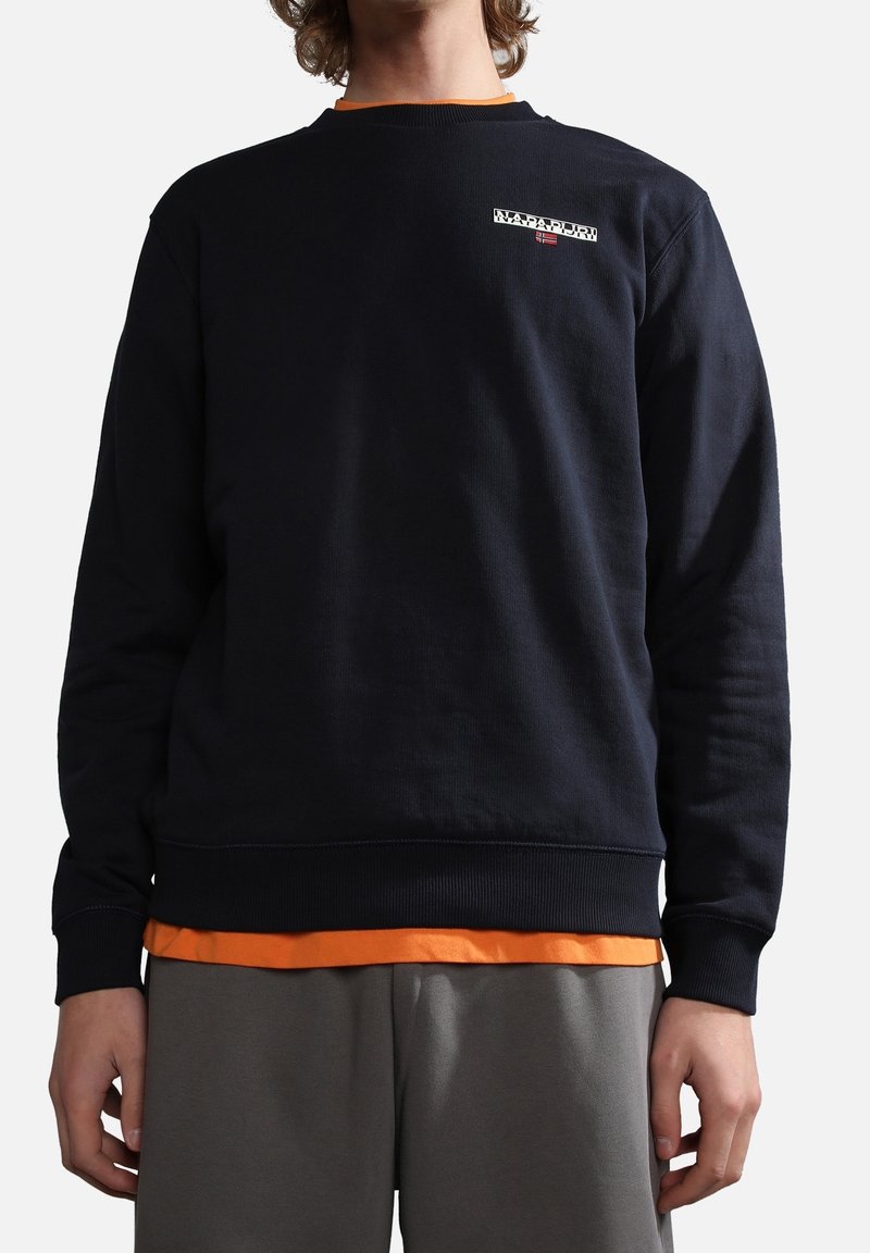 Sudadera azul marino con escote de barco, puños acanalados y dobladillo. Presenta un pequeño logo en el pecho y está superpuesta con una camiseta naranja.