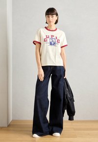 Λευκό βαμβακερό μπλουζάκι με κόκκινο ριγέ λαιμό και μανίκια, διακοσμημένο με γραφική εκτύπωση. Σκούρο μπλε φαρδύ παντελόνι, συνδυασμένο με λευκά παπούτσια.