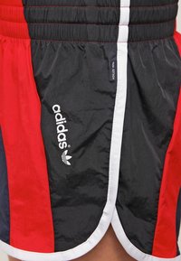 Pantaloni sportivi neri e rossi con vita elastica, dettagli bianchi e logo ricamato. Realizzati in tessuto leggero e testurizzato.