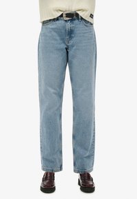Jeans de mezclilla de pierna recta en un azul claro con una textura ligeramente deslavada. Combinados con mocasines burdeos oscuros para un contraste.