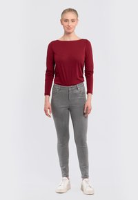 Red long-sleeve top paired with slim-fit grey jeans and white sneakers. The top features a boat neckline and smooth texture.